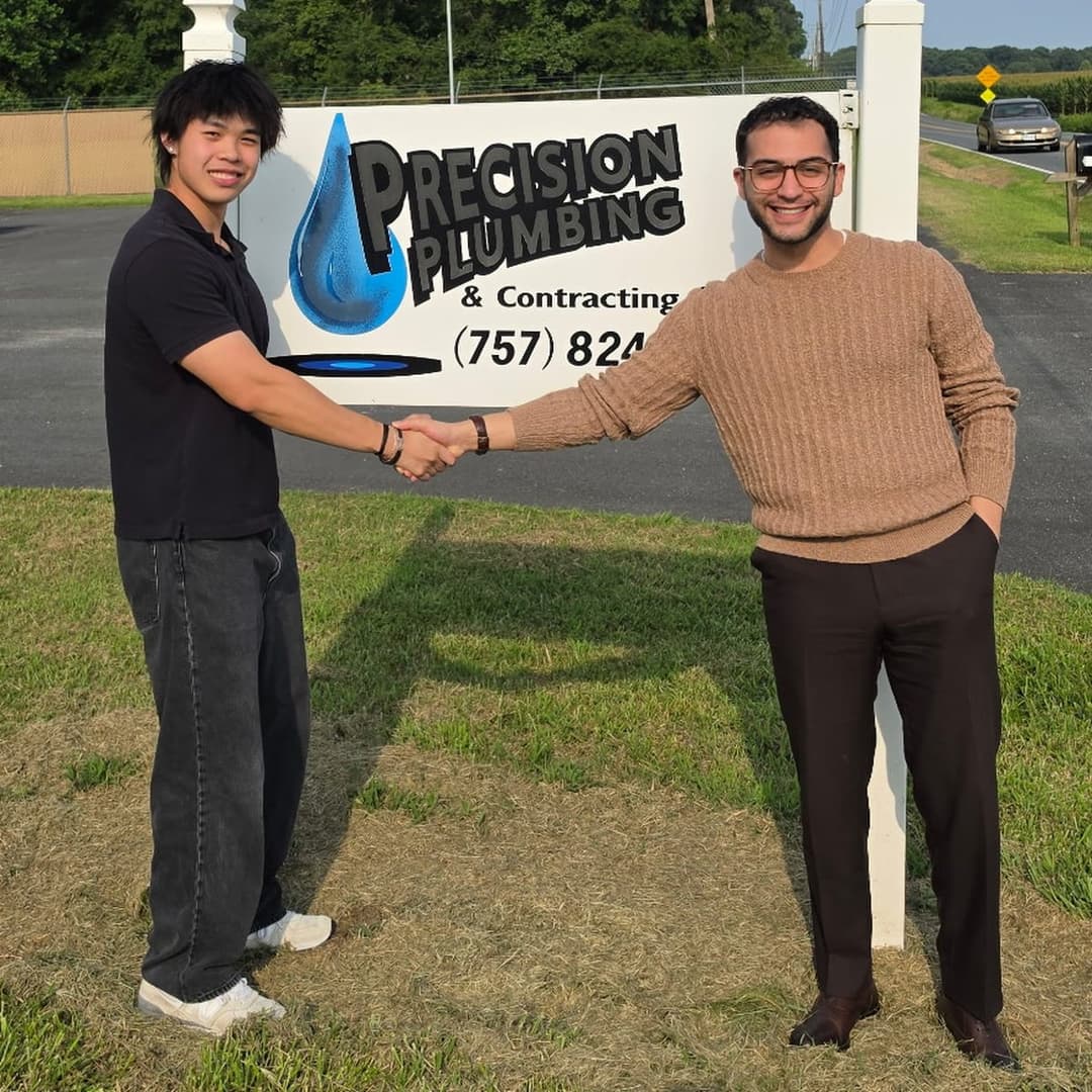 Kyle Vitayanuvatti and Elias Youssef shaking hands in front of the Precision Plumbing sign on closing day.